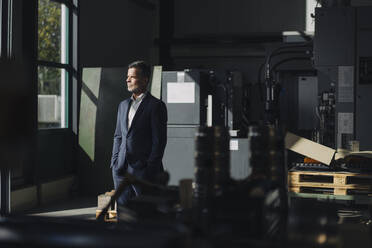 Businessman in a factory looking out of window - KNSF07904