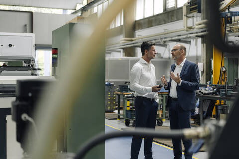 Zwei Geschäftsleute unterhalten sich in einer Fabrik, lizenzfreies Stockfoto