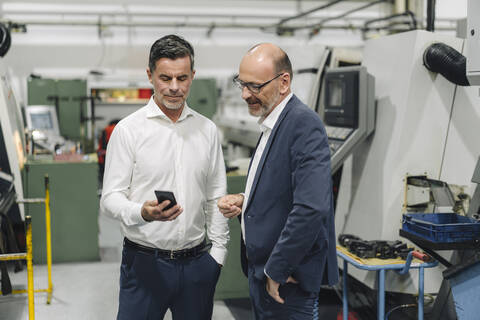 Two businessmen using smartphone in a factory stock photo