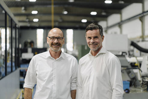 Porträt von zwei lächelnden Geschäftsleuten in einer Fabrik - KNSF07917