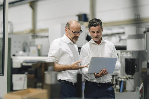 Zwei Geschäftsleute benutzen einen Laptop in einer Fabrik - KNSF07919