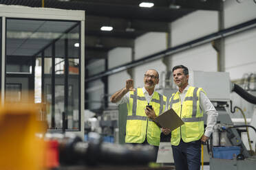 Two men in reflective vests talking in a factory - KNSF07920