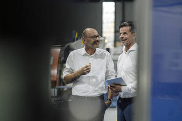 Zwei lächelnde Geschäftsleute unterhalten sich in einer Fabrik - KNSF07921