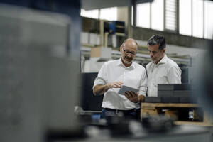 Zwei Geschäftsleute benutzen ein Tablet in einer Fabrik - KNSF07923