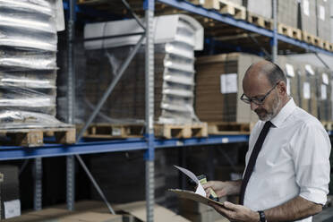 Man with clipboard and scanner in factory warehouse - KNSF07930