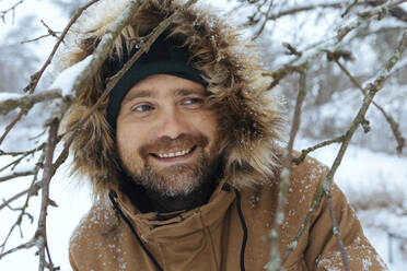 Porträt eines lächelnden Mannes mit Kapuzenjacke im Winter - KNTF04424