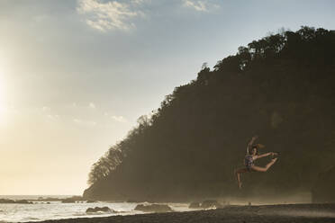 Teenage girl practicing gymnastic on the beach by sunset, Jaco Beach, Costa Rica - AMUF00015
