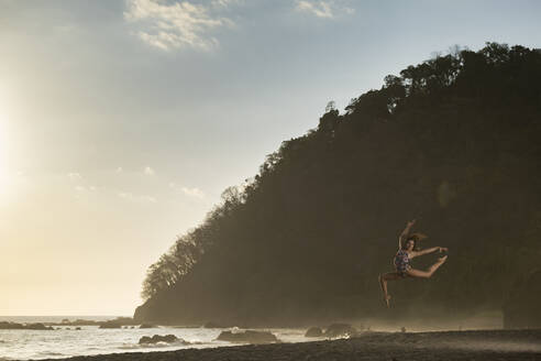 Teenager-Mädchen übt Gymnastik am Strand bei Sonnenuntergang, Jaco Beach, Costa Rica - AMUF00015