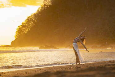 Teenage girl practicing gymnastic at seafront by sunset, Jaco Beach, Costa Rica - AMUF00016