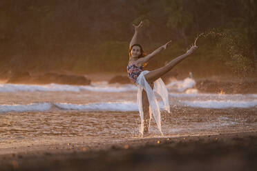 Porträt eines jugendlichen Mädchens, das bei Sonnenuntergang am Strand von Jaco, Costa Rica, Gymnastik übt - AMUF00017