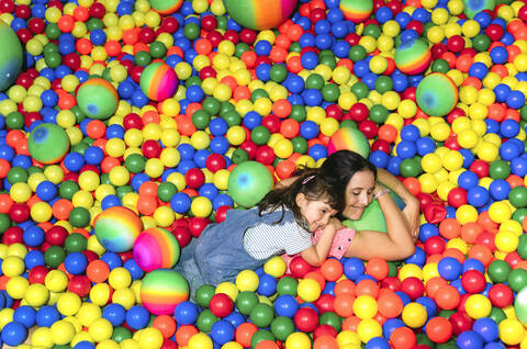 Happy woman lying with her little daughter among many colourful balls stock photo