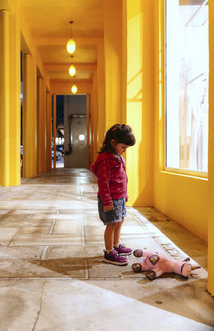 Trauriges kleines Mädchen, das ein auf dem Boden liegendes Spielzeug-Einhorn betrachtet, lizenzfreies Stockfoto