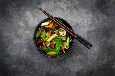 Pair of chopsticks and bowl of ready-to-eat miso soup with udon noodles, tofu, sugar snap peas, paprika, carrots, mu-err mushrooms, scallion and cilantro - LVF08664