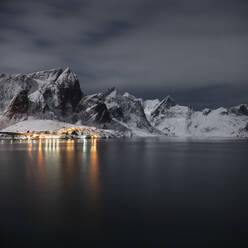Village lights shine on moonlit winter night near Reine, Moskenesøy, Lofoten Islands, Norway - CAVF76096