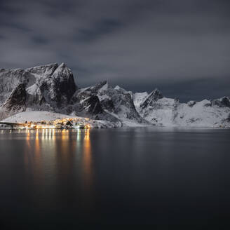 Dorflichter leuchten in einer mondhellen Winternacht in der Nähe von Reine, Moskenesøy, Lofoten, Norwegen - CAVF76096