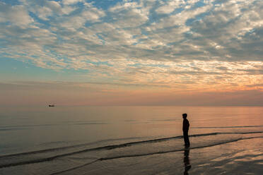 Ein Junge am Strand steht und beobachtet das Boot - CAVF76144