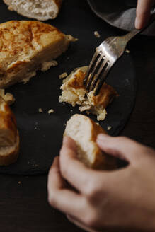 Nahaufnahme einer Frau, die mit einer Gabel ein spanisches Kartoffelomelett isst, in der anderen Hand ein Stück Brot. - CAVF76163