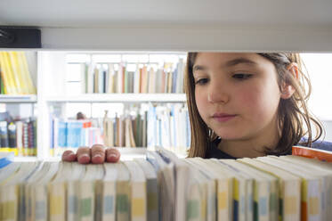 Junges Mädchen wählt Bücher aus dem Bücherregal der Bibliothek aus - CAVF76173