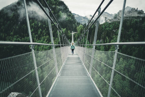 Junge Frau beim Wandern über eine Hängeseilbrücke in alpiner Umgebung - CAVF76186