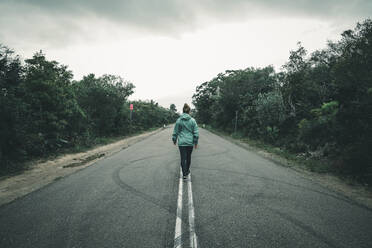 Rückansicht einer jungen Frau, die auf der Landstraße läuft - CAVF76194