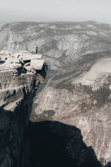 Junge Frau steht auf dem Half Dome und schaut über eine Klippe - CAVF76199