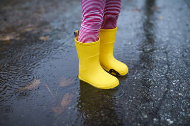 Eine Nahaufnahme der Regenstiefel eines Kindes in einer Pfütze. - CAVF76240