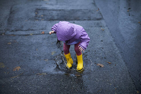 Ein kleines Mädchen, das an einem regnerischen Tag in Pfützen planscht. - CAVF76241