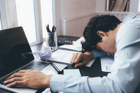 Ein junger Geschäftsmann, der hart arbeitet und am Schreibtisch schläft. - CAVF76281