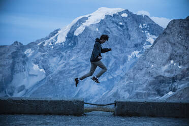 Junger Mann springt auf eine Mauer am Stilfserjoch, Italien - DHEF00130