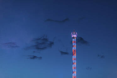 Deutschland, Bayern, München, Low angle view of Bayern Tower chain swing ride glowing against sky at dusk - MMAF01294