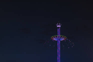 Deutschland, Bayern, München, Low angle view of Bayern Tower chain swing ride glowing against sky at night - MMAF01295