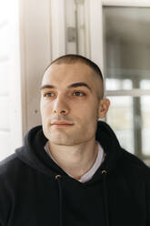 Portrait of pensive young man with shaved head looking at distance - KMKF01230