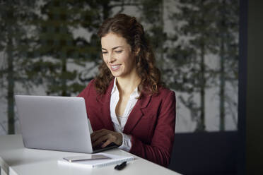 Lächelnde Geschäftsfrau mit Laptop im Büro - RBF07077