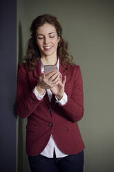 Porträt einer lächelnden Geschäftsfrau, die im Büro ein Mobiltelefon benutzt - RBF07081