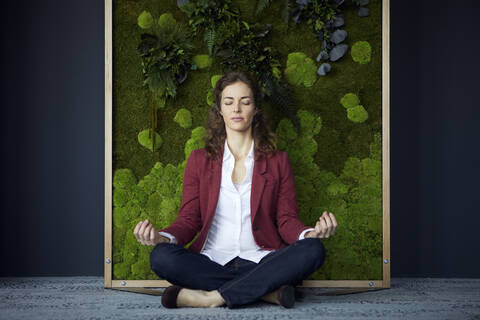 Businesswoman sitting on the floor in green office practicing yoga stock photo