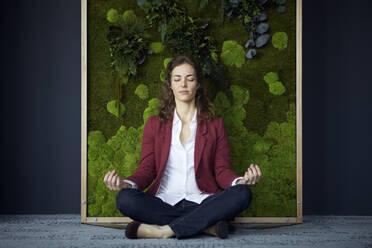 Businesswoman sitting on the floor in green office practicing yoga - RBF07084