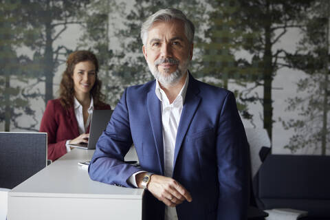 Porrait of smiling businessman in office with businesswoman in background stock photo