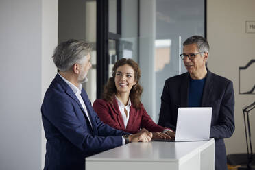 Two businessmen and businesswoman working together on laptop in office - RBF07109