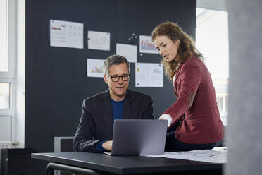 Geschäftsmann und Geschäftsfrau arbeiten zusammen an einem Laptop im Büro - RBF07129