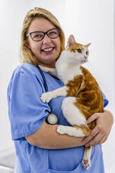 Porträt einer lächelnden Frau, die eine Katze in einer Tierklinik hält - DLTSF00603