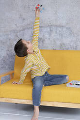 Junge spielt und experimentiert mit molekularen Modellen auf gelber Couch sitzend - HMEF00783
