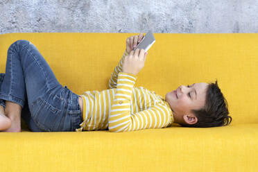 Boy playing with tablet on yellow couch - HMEF00790