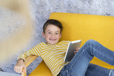 Boy playing with tablet on yellow couch - HMEF00793