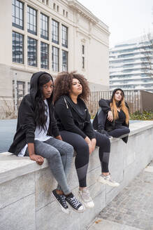 Drei sportliche junge Frauen sitzen auf einer Mauer in der Stadt - MEUF00029