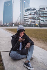 Junge Frau benutzt Smartphone in der Stadt in der Dämmerung - MEUF00039