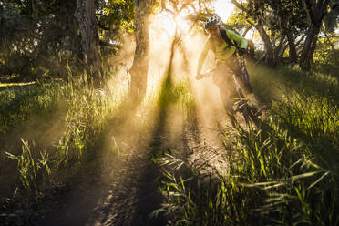 Weibliche Mountainbikerin fährt bei Sonnenuntergang auf einem Feldweg, Fort Ord National Monument Park, Monterey, Kalifornien, USA - MSUF00234