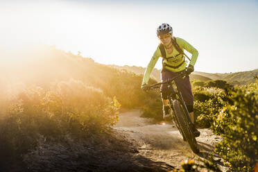 Weibliche Mountainbikerin fährt bei Sonnenuntergang auf einem Feldweg, Fort Ord National Monument Park, Monterey, Kalifornien, USA - MSUF00235