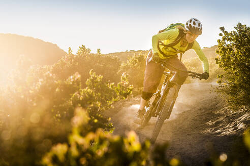 Weibliche Mountainbikerin fährt bei Sonnenuntergang auf einem Feldweg, Fort Ord National Monument Park, Monterey, Kalifornien, USA - MSUF00237