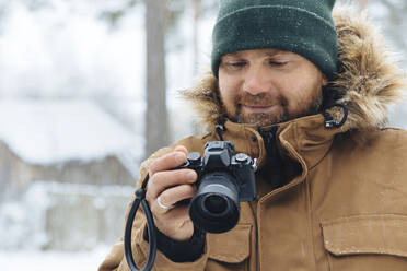 Portrait of smiling man looking at digital camera in winter - KNTF04481