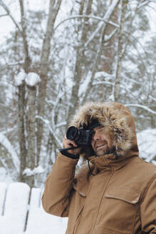 Bärtiger Mann fotografiert mit Digitalkamera im Winterwald - KNTF04490